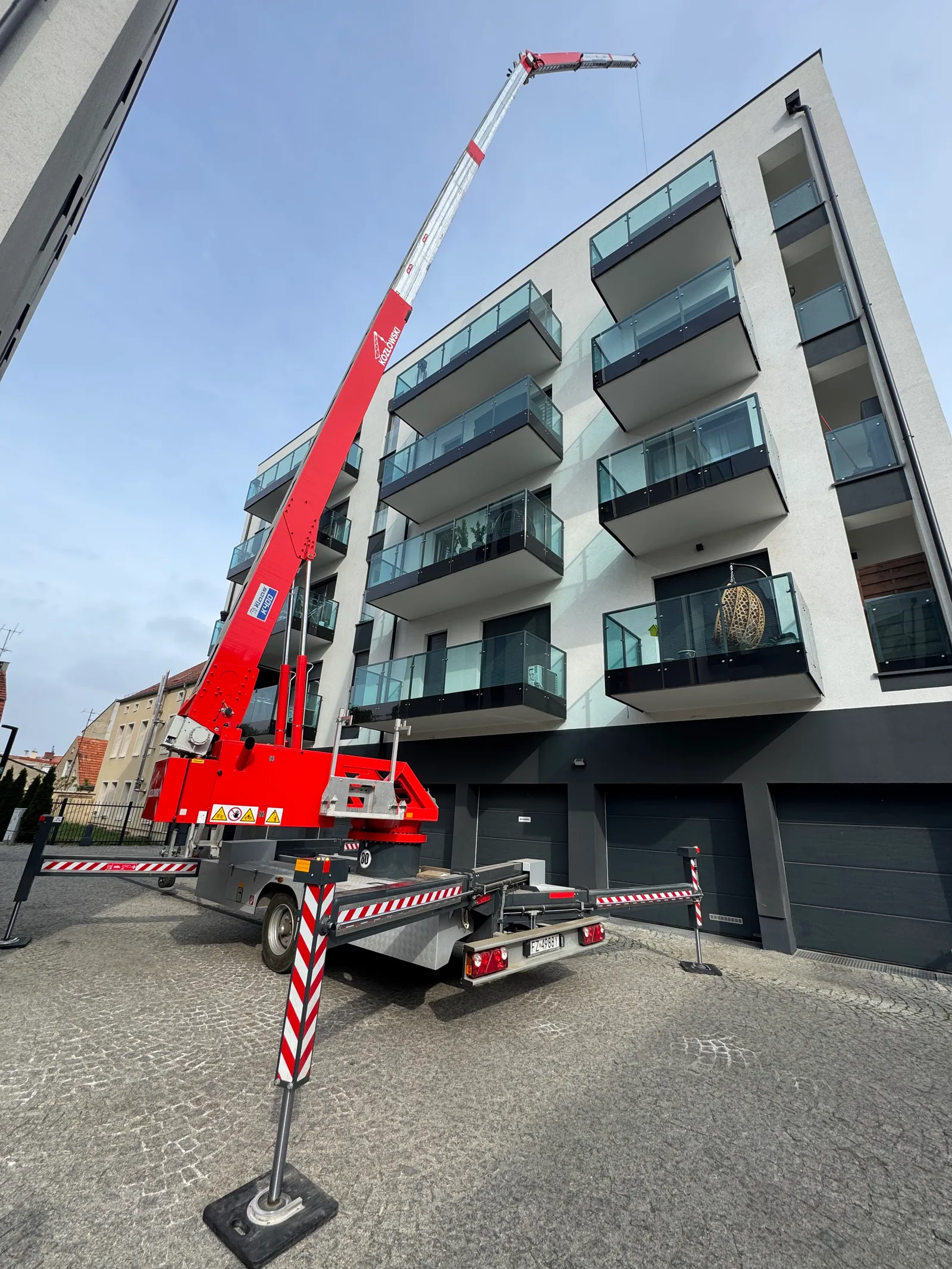 Żuraw dekarski Klaas K400 Kozłowskiego na osiedlu — hydrauliczny jib przełamany nad dachem bloku z balkonami