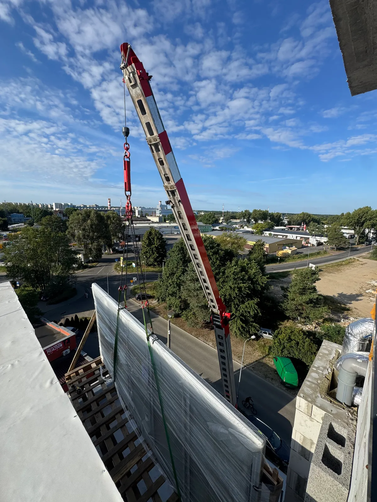 Hydrauliczny jib żurawia Klaas K400 opuszcza ładunek na dach, widok z góry na panoramę miasta