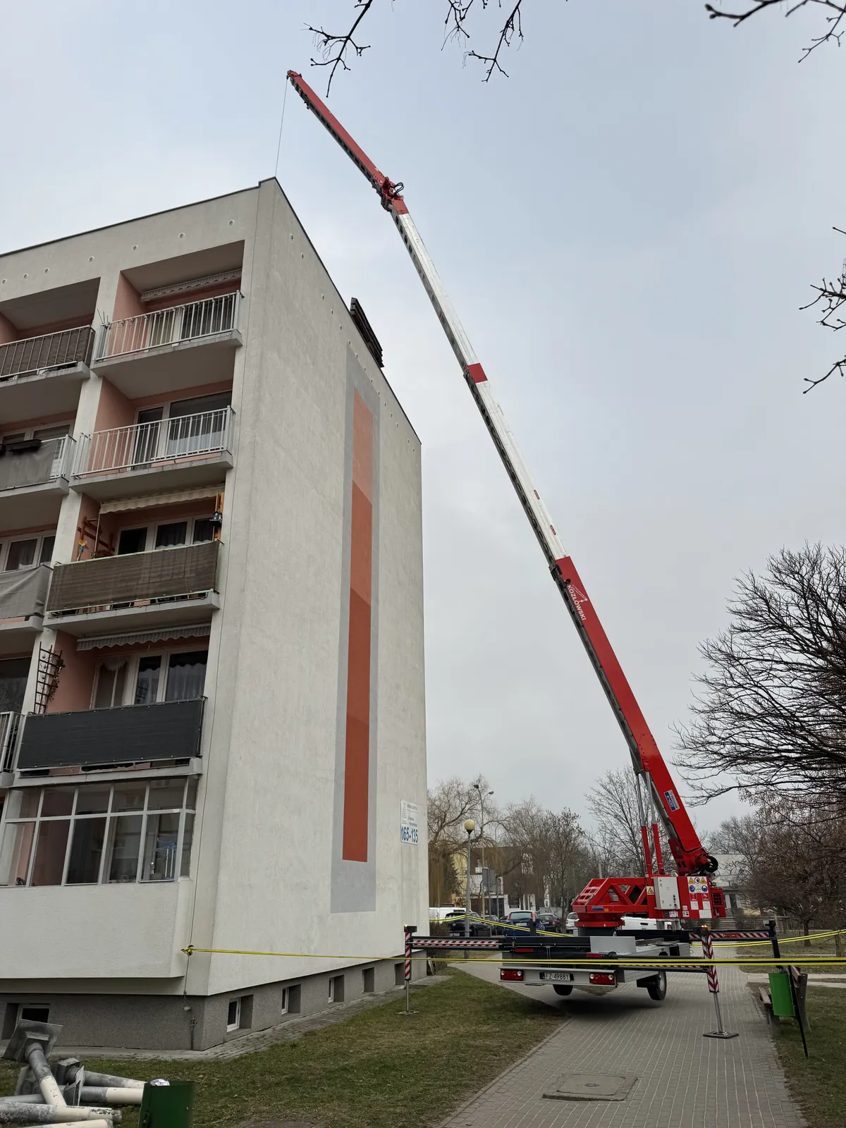 Żuraw dekarski podaje materiał na dach bloku prosto z chodnika