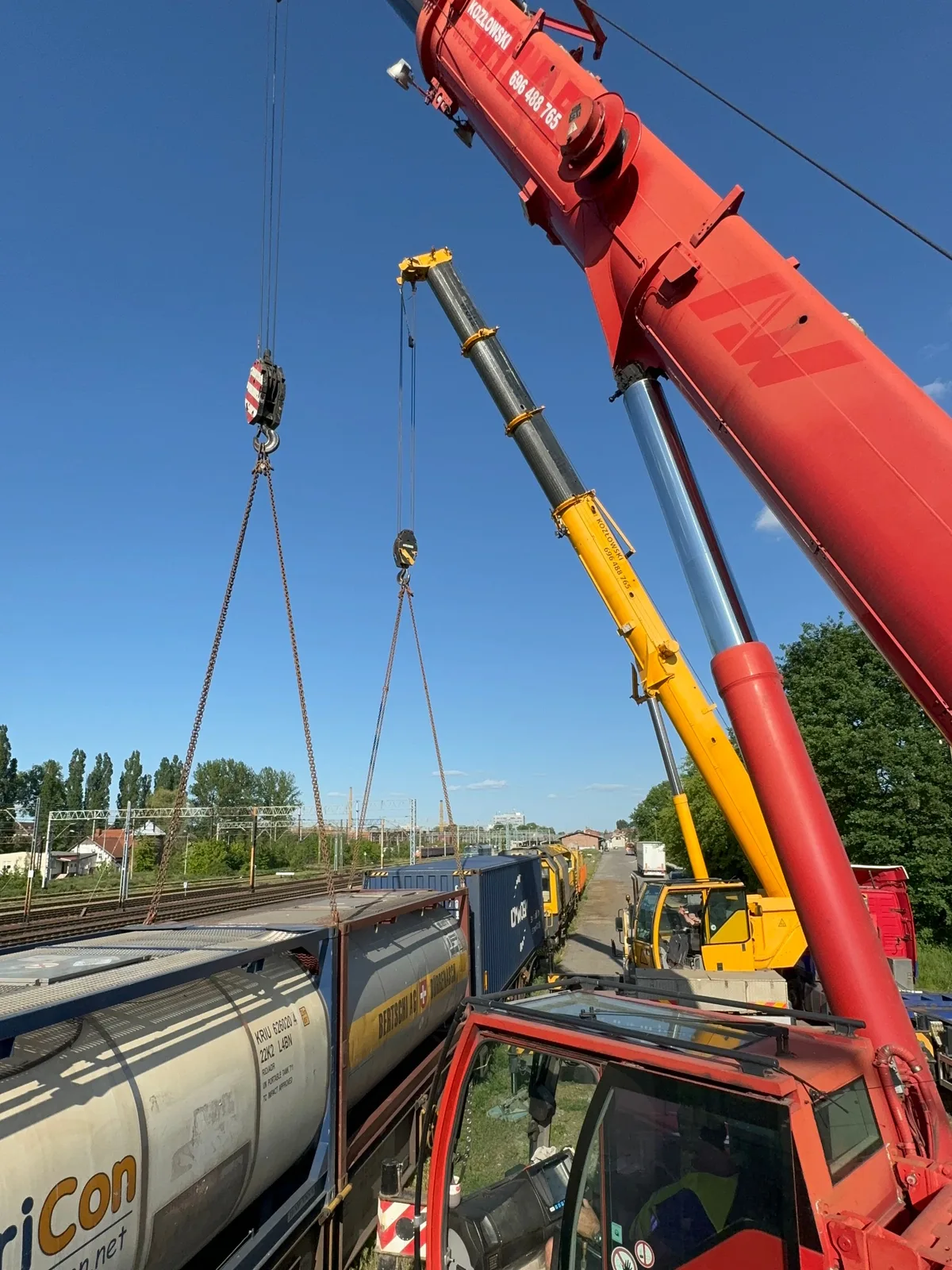 Dwa żurawie samojezdne Liebherr Kozłowskiego pracują razem nad wagonami z cysternami na bocznicy kolejowej