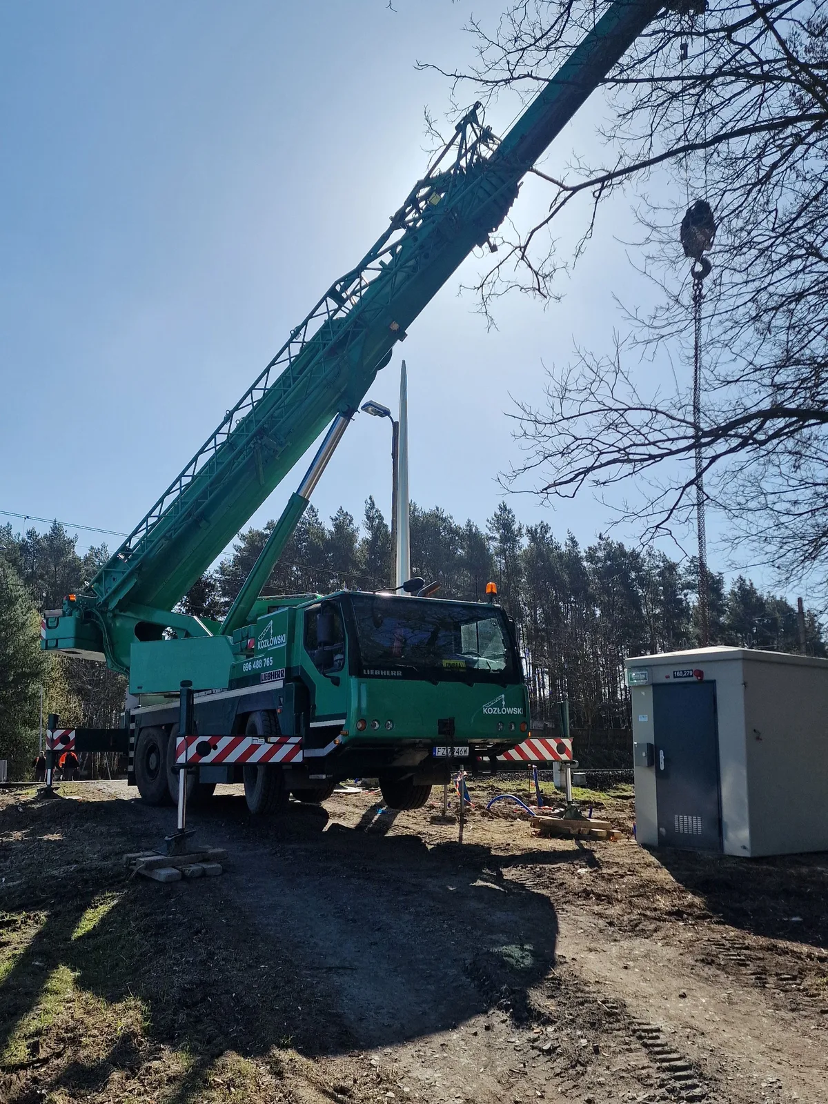 Zielony Liebherr LTM 1055-3.2 z kratowym jibem pracuje przy stacji transformatorowej pod lasem