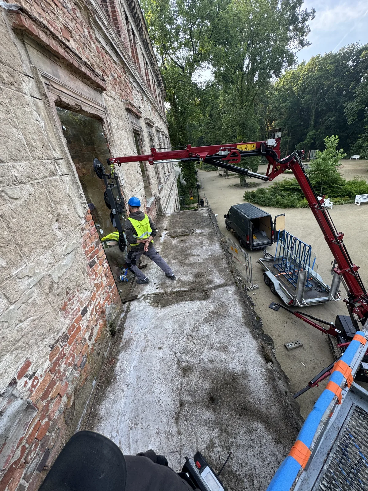 Chwytak próżniowy z szybą przy oknie zabytkowego pałacu — widok z góry na park i stojaki ze szkłem
